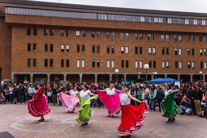 Students in brightly colored full skirts of pink, magenta and green dancing in the plaza in red square.